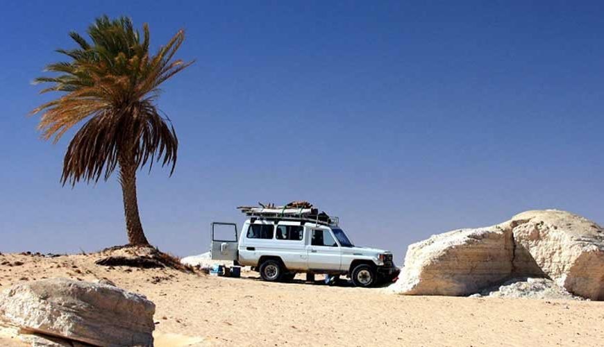 Off-road vehicle driving through white chalk formations during a White Desert safari in Egypt.