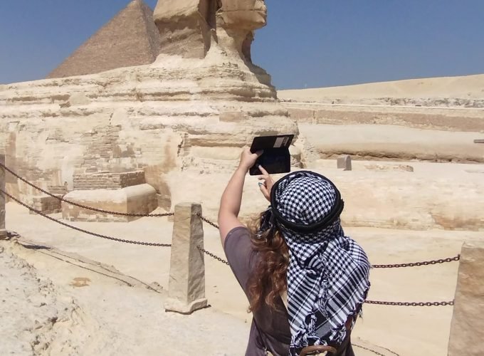 Une femme de dos portant un keffieh traditionnel photographie le Grand Sphinx de Gizeh avec son smartphone, une étape clé du voyage Pyramides depuis Sharm El-Sheikh