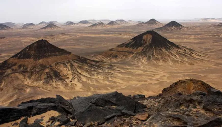 Dunas de arena oscura en el Desierto Negro de Egipto bajo un cielo despejado.