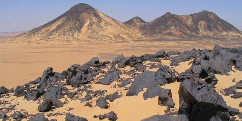 Dunas de areia escura no Deserto Negro do Egito sob um céu limpo.