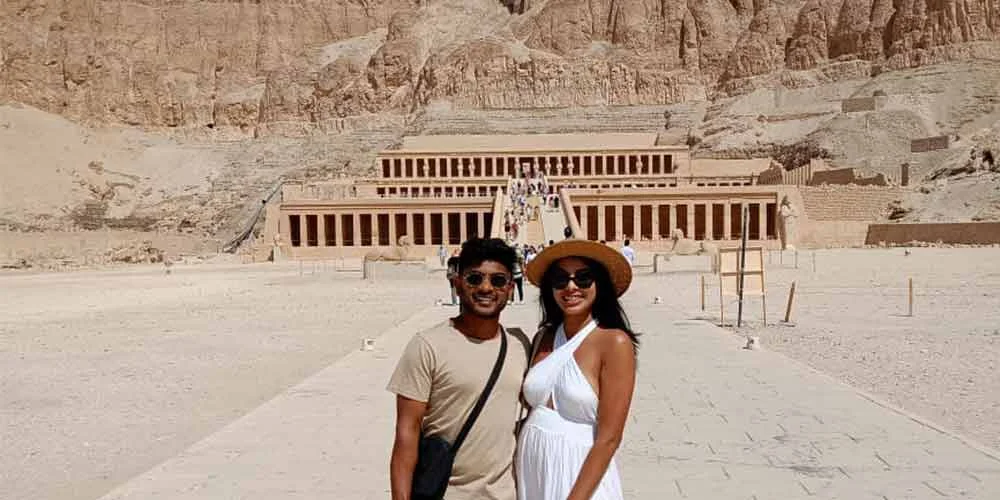 Una pareja frente al Templo de Hatshepsut en Egipto, con su fachada escalonada y columnas monumentales.