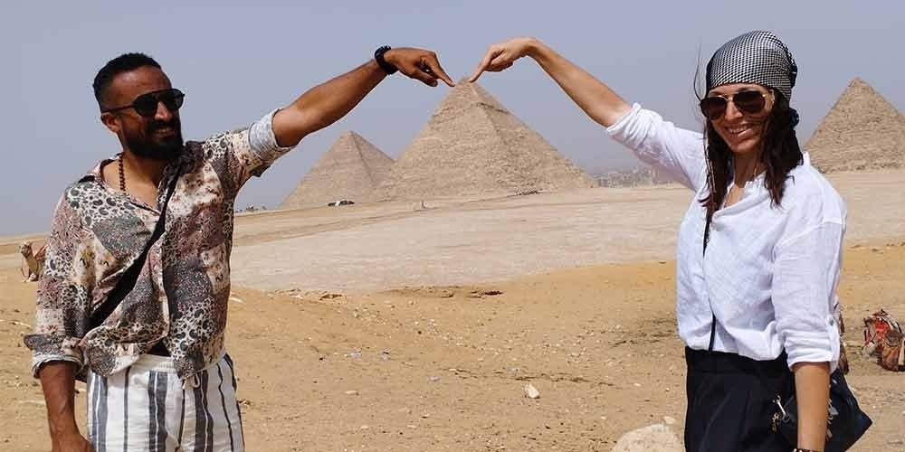 A couple taking a funny photo in front of the pyramids, with their fingers.