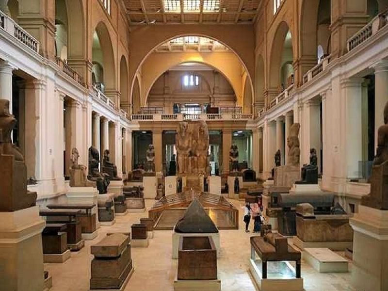 An interior view of the Egyptian Museum’s grand hall filled with ancient statues, stone sarcophagi, and historical monuments under high arched ceilings, perfect for an Egypt Vacation