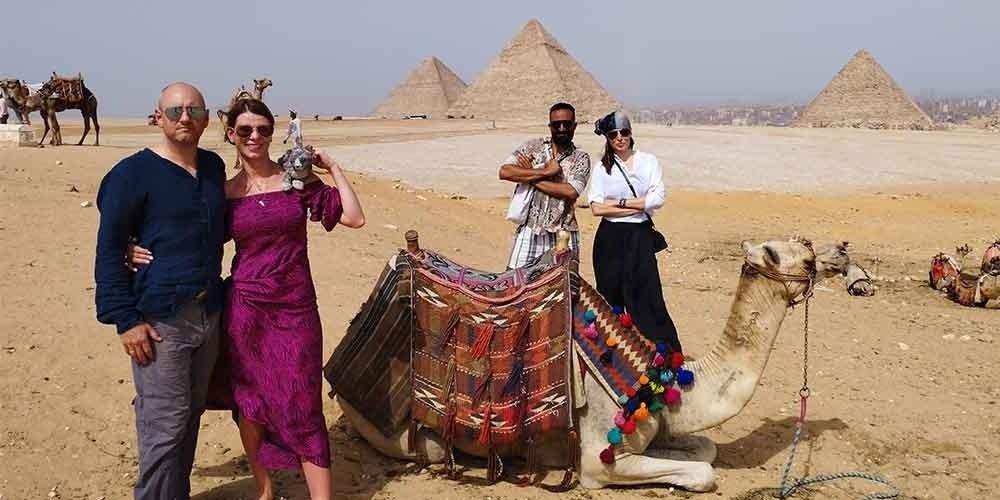 3 Tourists in Giza Pyramids Area with a camel and enjoying their time.
