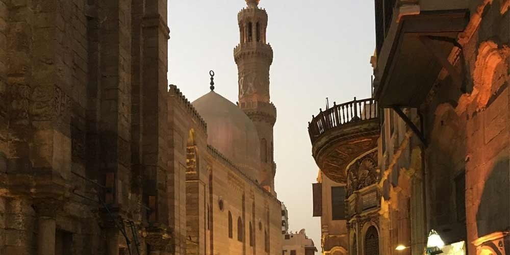 Beco movimentado do bazar Khan El Khalili, com lojas tradicionais, lanternas coloridas e pessoas caminhando.