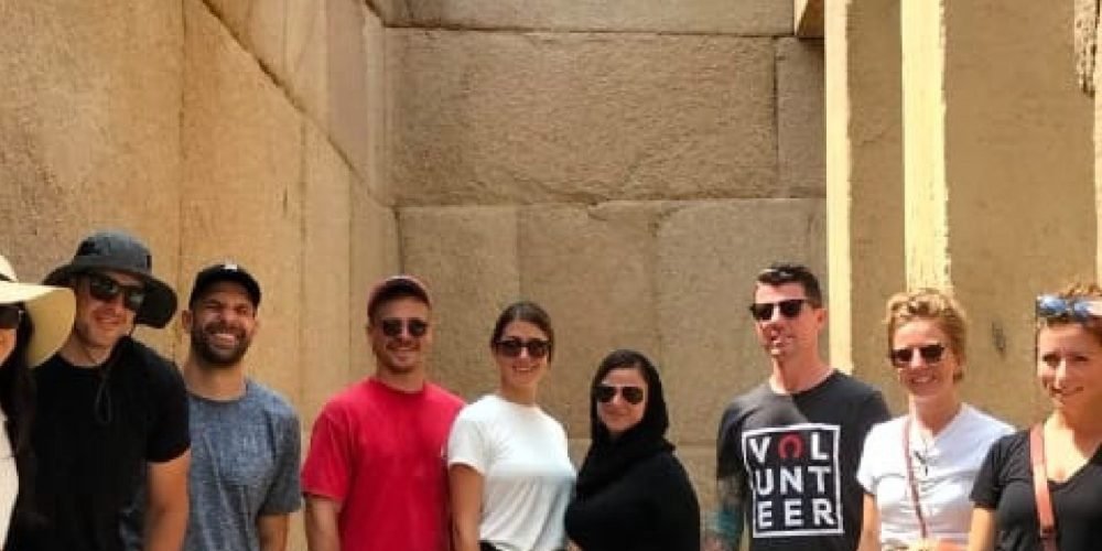 Grupo de turistas sorrindo com as Pirâmides de Gizé ao fundo, no deserto do Egito.