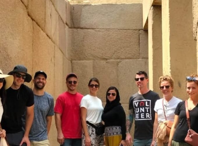 Grupo de turistas sorrindo com as Pirâmides de Gizé ao fundo, no deserto do Egito.