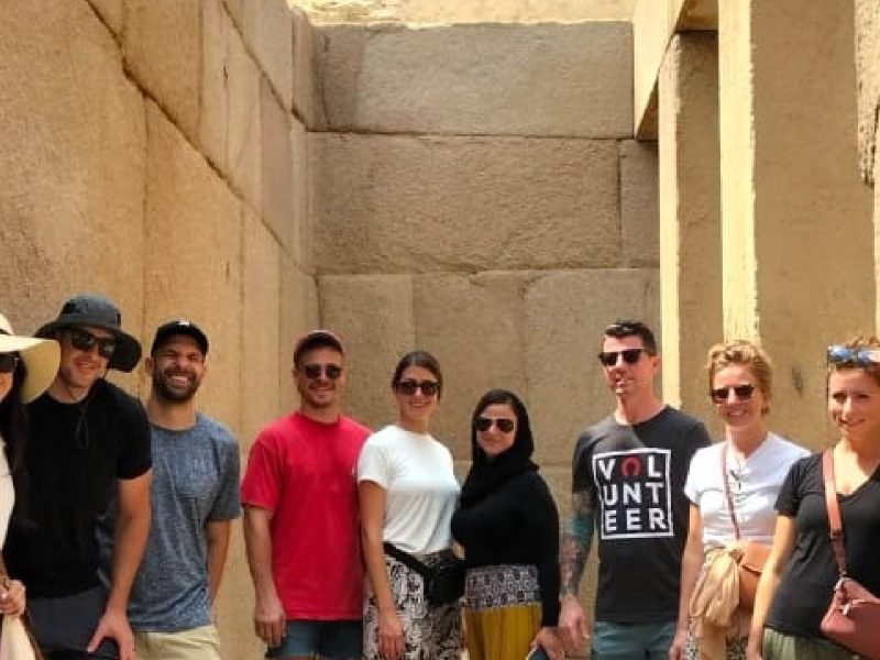 Grupo de turistas sorrindo com as Pirâmides de Gizé ao fundo, no deserto do Egito.