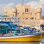 Bateaux de pêche colorés amarrés dans le port d’Alexandrie, avec la citadelle de Qaitbay en arrière-plan.