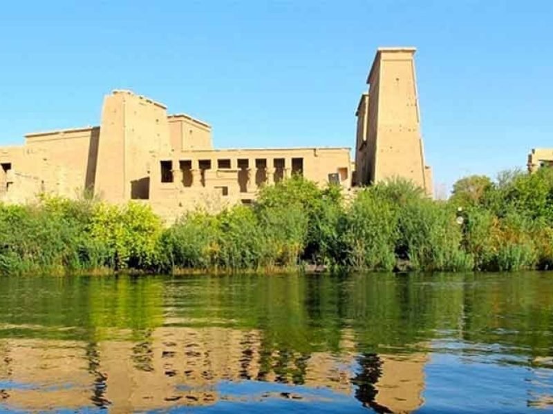Vista do Templo de Philae, em Assuã, com seus pórticos e colunas refletidos nas águas do rio Nilo.