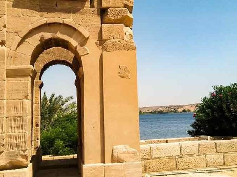 Vista do Templo de Philae, em Assuã, com seus pórticos e colunas refletidos nas águas do rio Nilo.