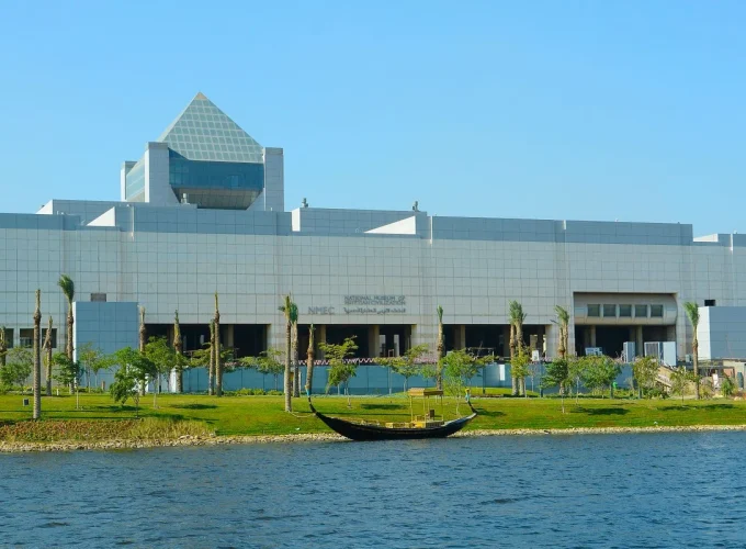 The National Museum of Egyptian Civilization beside a calm lake, surrounded by trees and green landscape