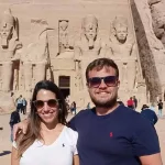 Day tour to Abu Simbel Temple2 Two tourists standing in front of Abu Simbel Temple under bright sunlight.