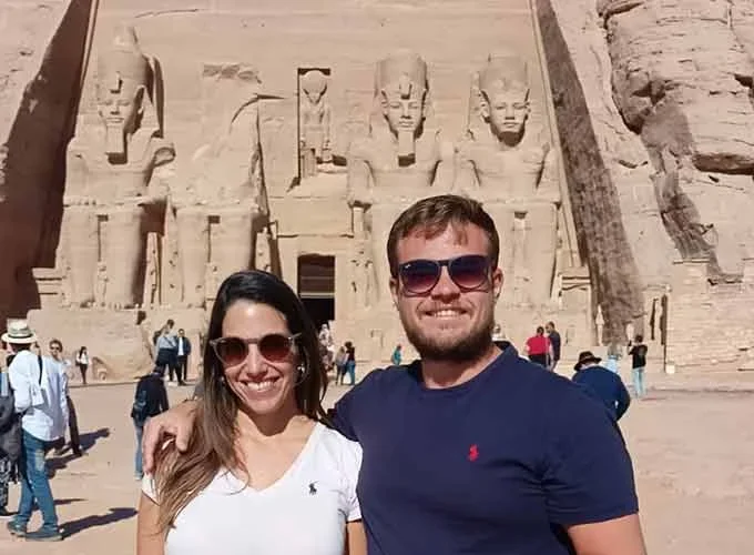 Two tourists standing in front of Abu Simbel Temple under bright sunlight.