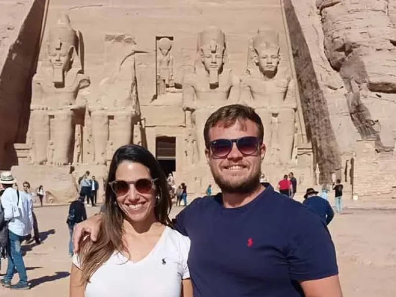 Two tourists standing in front of Abu Simbel Temple under bright sunlight.