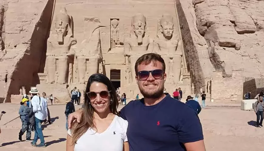 Two tourists standing in front of Abu Simbel Temple under bright sunlight.