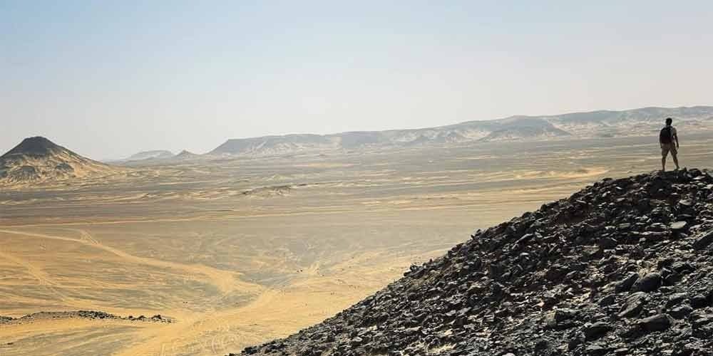 Voyageur admirant le panorama entre le désert blanc et l'oasis de Bahariya depuis une colline rocheuse.