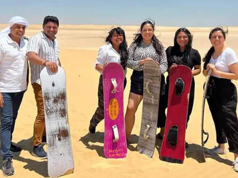 A group of people enjoying sandboarding on desert dunes in Fayum