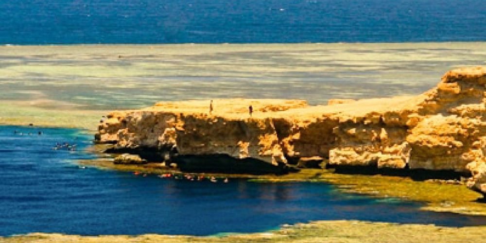 Vista panorâmica da costa rochosa do Parque Nacional de Ras Mohammed com águas rasas azul-turquesa e o mar aberto ao fundo.
