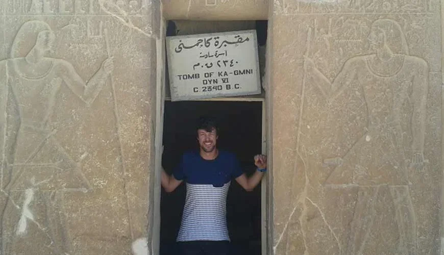 A tourist taking a photo inside the tomb of Kagmni at Saqqara, showing ancient Egyptian wall reliefs.