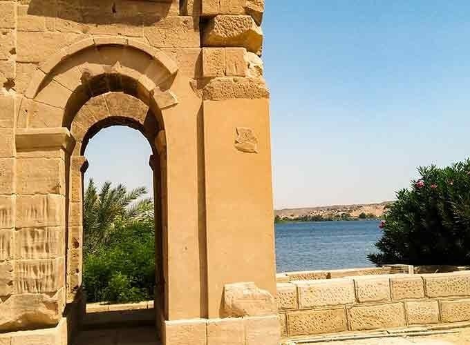 Ancient stone archway overlooking the Nile River with palm trees and clear blue sky in Egypt.