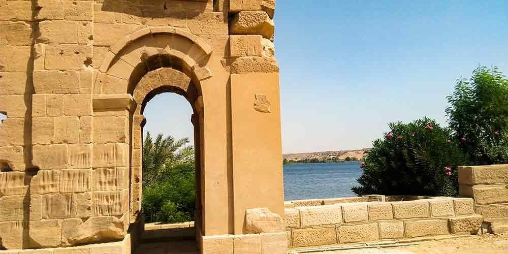 Ancient stone archway overlooking the Nile River with palm trees and clear blue sky in Egypt.
