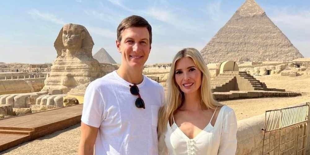 A smiling man and woman in white summer outfits posing in front of the Great Sphinx and the Pyramids of Giza during their Low Budget Egypt Tour. The ancient limestone monuments and desert sands stretch behind them under a bright, hazy sky at this world-famous archaeological site