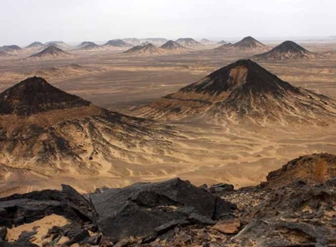 Caminho estreito entre dunas negras no Deserto Negro ao pôr do sol.