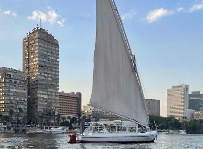 Feluca no rio Nilo passando por palmeiras, vilarejos e águas tranquilas.
