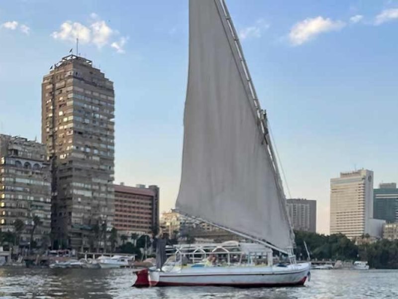 Feluca no rio Nilo passando por palmeiras, vilarejos e águas tranquilas.
