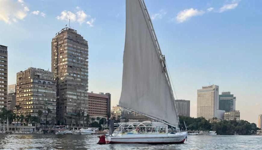 Feluca no rio Nilo passando por palmeiras, vilarejos e águas tranquilas.