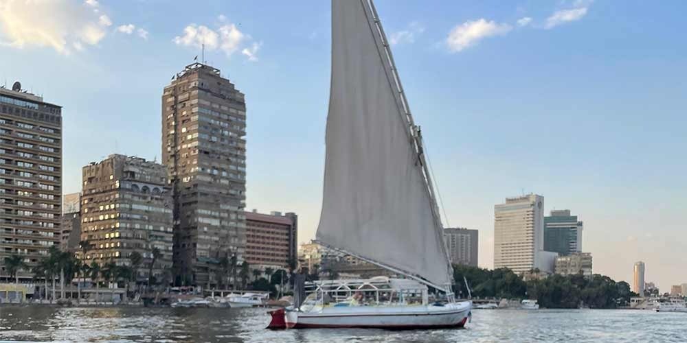 Feluca no rio Nilo passando por palmeiras, vilarejos e águas tranquilas.