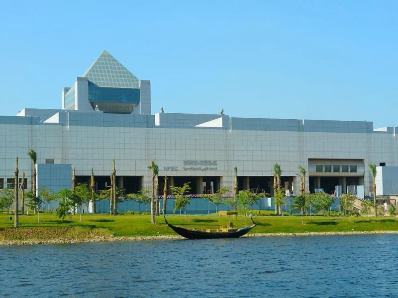The National Museum of Egyptian Civilization beside a calm lake, surrounded by trees and green landscape
