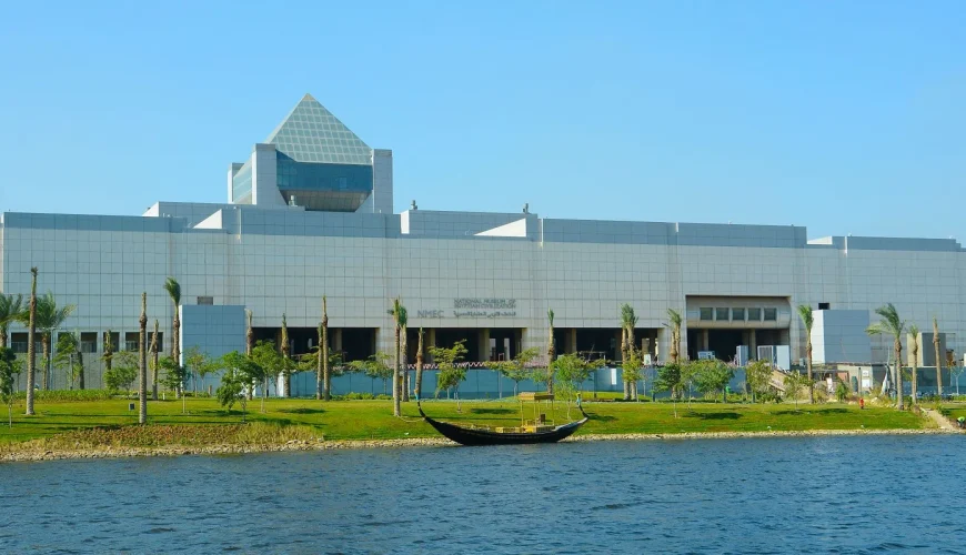 The National Museum of Egyptian Civilization beside a calm lake, surrounded by trees and green landscape