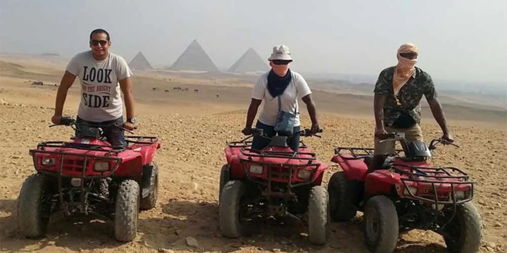 A person riding a quad bike near the Giza Pyramids, kicking up dust in the sand