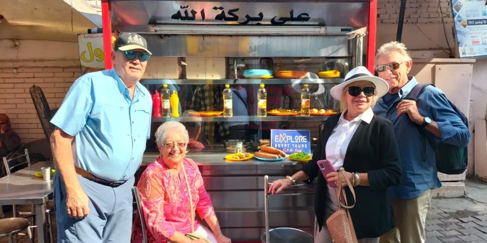 Group of friends taking a photo in front of a traditional Egyptian ful and falafel restaurant during their tour