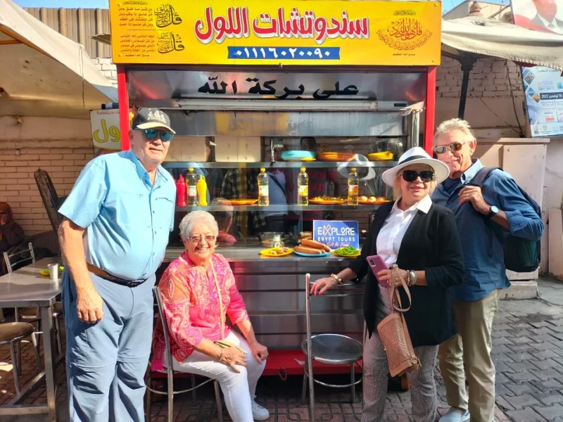 Group of friends taking a photo in front of a traditional Egyptian ful and falafel restaurant during their tour