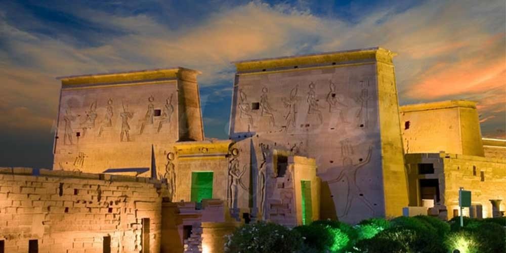 Templo de Philae iluminado à noite, refletindo suas colunas e hieróglifos no lago Nasser.
