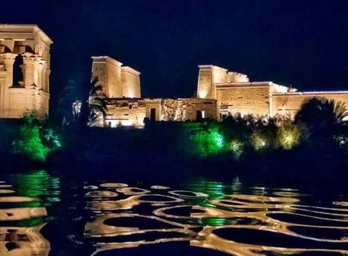 Visitantes apreciando o Templo de Philae à noite, com iluminação destacando detalhes arquitetônicos.