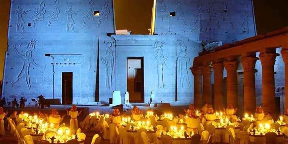 Vista panorâmica noturna do Templo de Philae, mostrando a magia do templo iluminado sobre as águas.