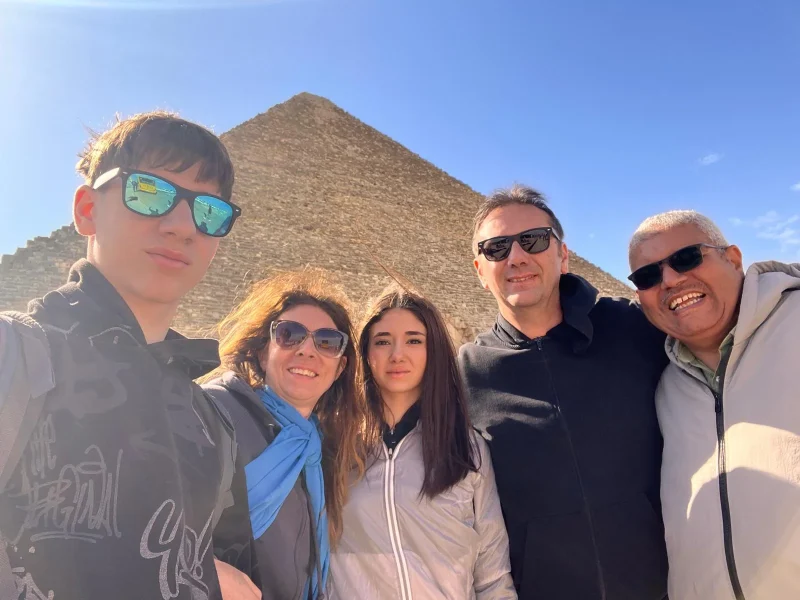 Una familia de cuatro personas toma una foto con su guía con las pirámides.
