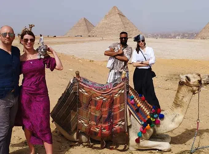 Un grupo de turistas posando con un camello frente a las Pirámides de Guiza.
