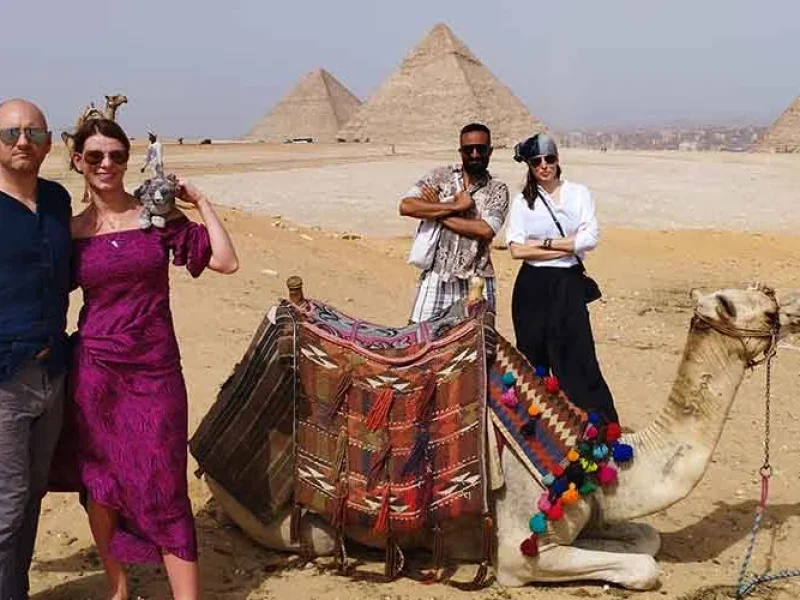Un grupo de turistas posando con un camello frente a las Pirámides de Guiza.
