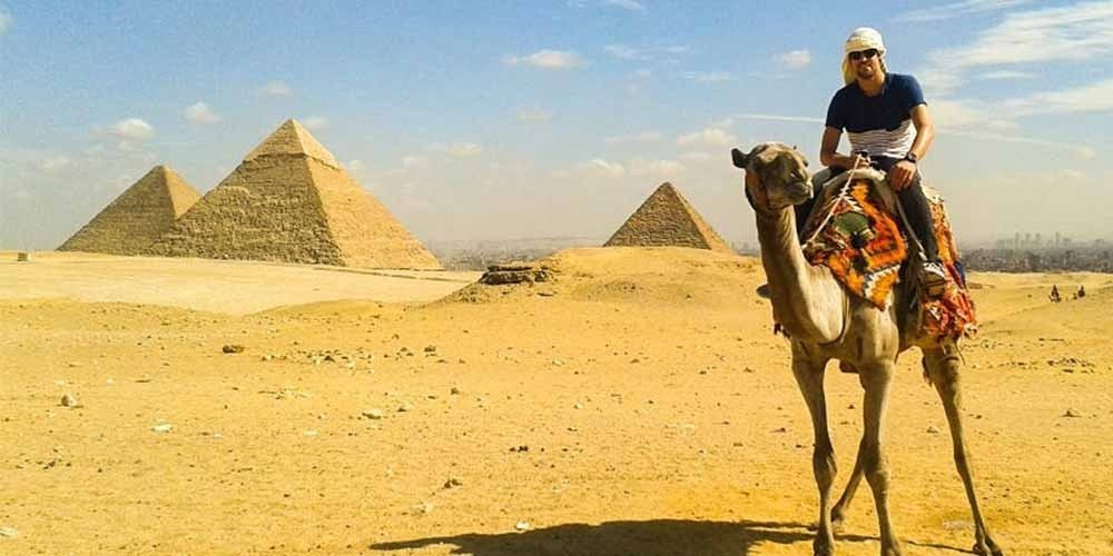 Un touriste à dos de chameau devant les trois pyramides de Gizeh, une activité typique d'une journée depuis la porte de port Said au Caire