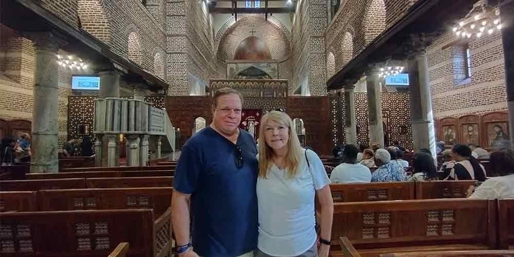 Un couple de touristes posant à l'intérieur d'une église copte historique avec une architecture en briques et des boiseries sculptées lors d'une visite spéciale au Caire copte et à Khan el-Khalil