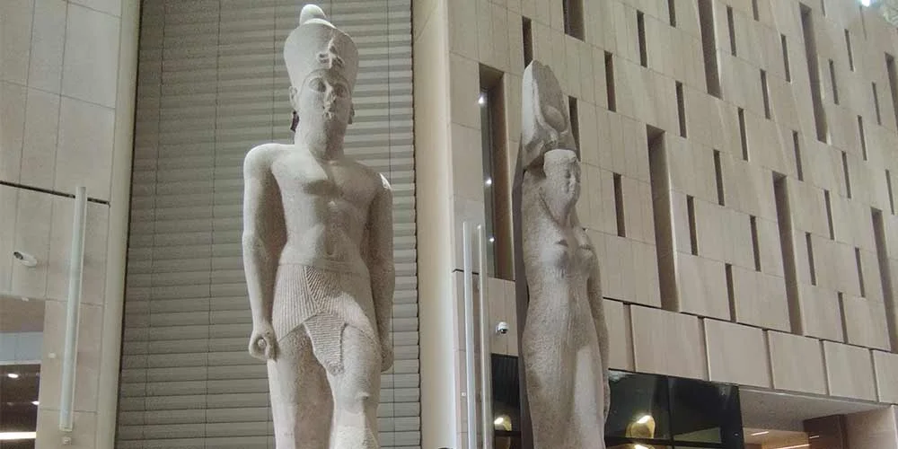 Two royal statues displayed on the grand staircase inside the Grand Egyptian Museum.