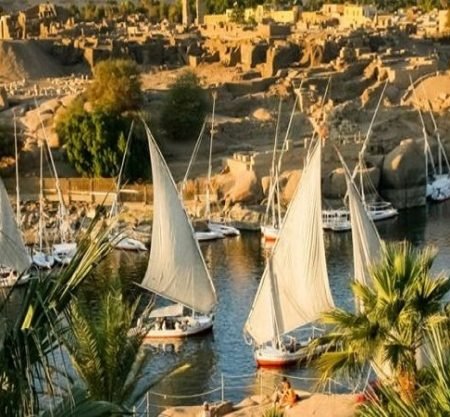 Plusieurs felouques traditionnelles aux voiles blanches naviguant sur le Nil à Assouan au coucher du soleil, une scène typique d'une Visite inoubliable a Souk du Assouan et village nubien