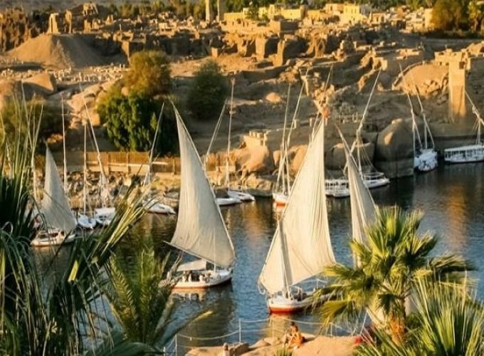 Plusieurs felouques traditionnelles aux voiles blanches naviguant sur le Nil à Assouan au coucher du soleil, une scène typique d'une Visite inoubliable a Souk du Assouan et village nubien