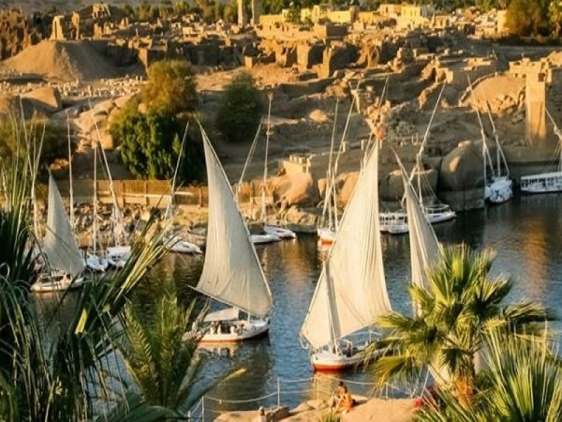 Plusieurs felouques traditionnelles aux voiles blanches naviguant sur le Nil à Assouan au coucher du soleil, une scène typique d'une Visite inoubliable a Souk du Assouan et village nubien