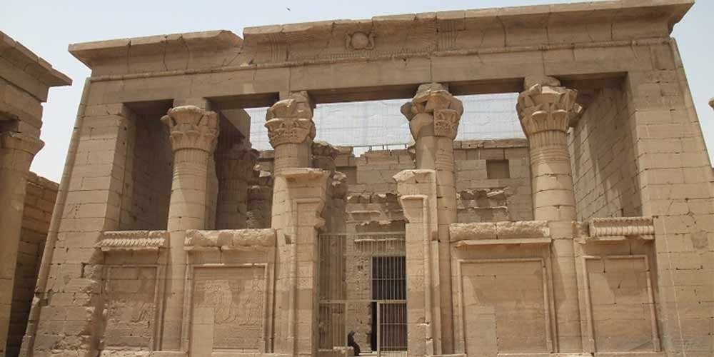 Une vue rapprochée de la structure en pierre du temple de Kalabsha montrant quatre colonnes massives avec des chapiteaux sculptés en forme de fleurs de lotus. Les colonnes soutiennent des blocs de pierre horizontaux sous un ciel clair, révélant les détails des gravures antiques lors d'une journée au musée nubien et temple de Kalabsha